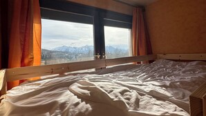Una cama con cabecera de madera y vistas a montañas a través de una ventana con cortinas.