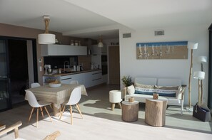 A modern living room with a dining area, a sofa, and a kitchen in the background.