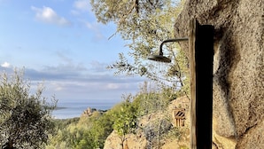A garden with a stone wall, a wooden bench, and a view of the sea. - Stone house with panoramic views over the bay of Figari, outdoor spa (Pianottoli-Caldarello)
