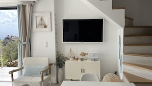 A modern living room with a white table, a TV mounted on the wall, and a staircase leading to an upper level. - Stone house with panoramic views over the bay of Figari, outdoor spa (Pianottoli-Caldarello)