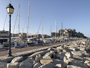 A marina with boats docked, a rocky shoreline, and a historic building in the background.