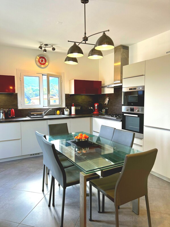 A modern kitchen with a glass dining table, stainless steel appliances, and a view of the outdoors. - CALVI new apt WIFI 3bedroom, 6 people, air-conditioned, 10mm beach (Calvi)