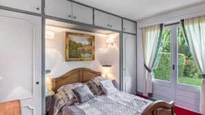 A bedroom with a bed, bedside lamps, a painting, and a view of greenery through a window. - 3 room apartment  (Megève)