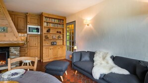 A cozy living room with a fireplace, a sofa, a bookshelf, and a dining area. - 3 room apartment  (Megève)