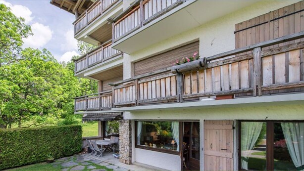 A multi-story building with balconies, a stone foundation, and a garden area with a patio. - 3 room apartment  (Megève)