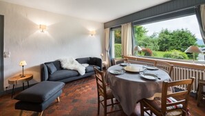 A cozy room with a sofa, a dining table set for two, and a view of greenery outside. - 3 room apartment  (Megève)