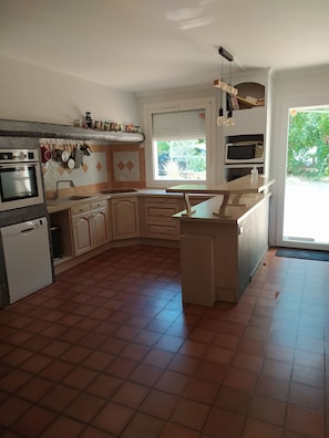 A kitchen with a built-in oven, microwave, and sink. There is a window with blinds, and a door leading outside.