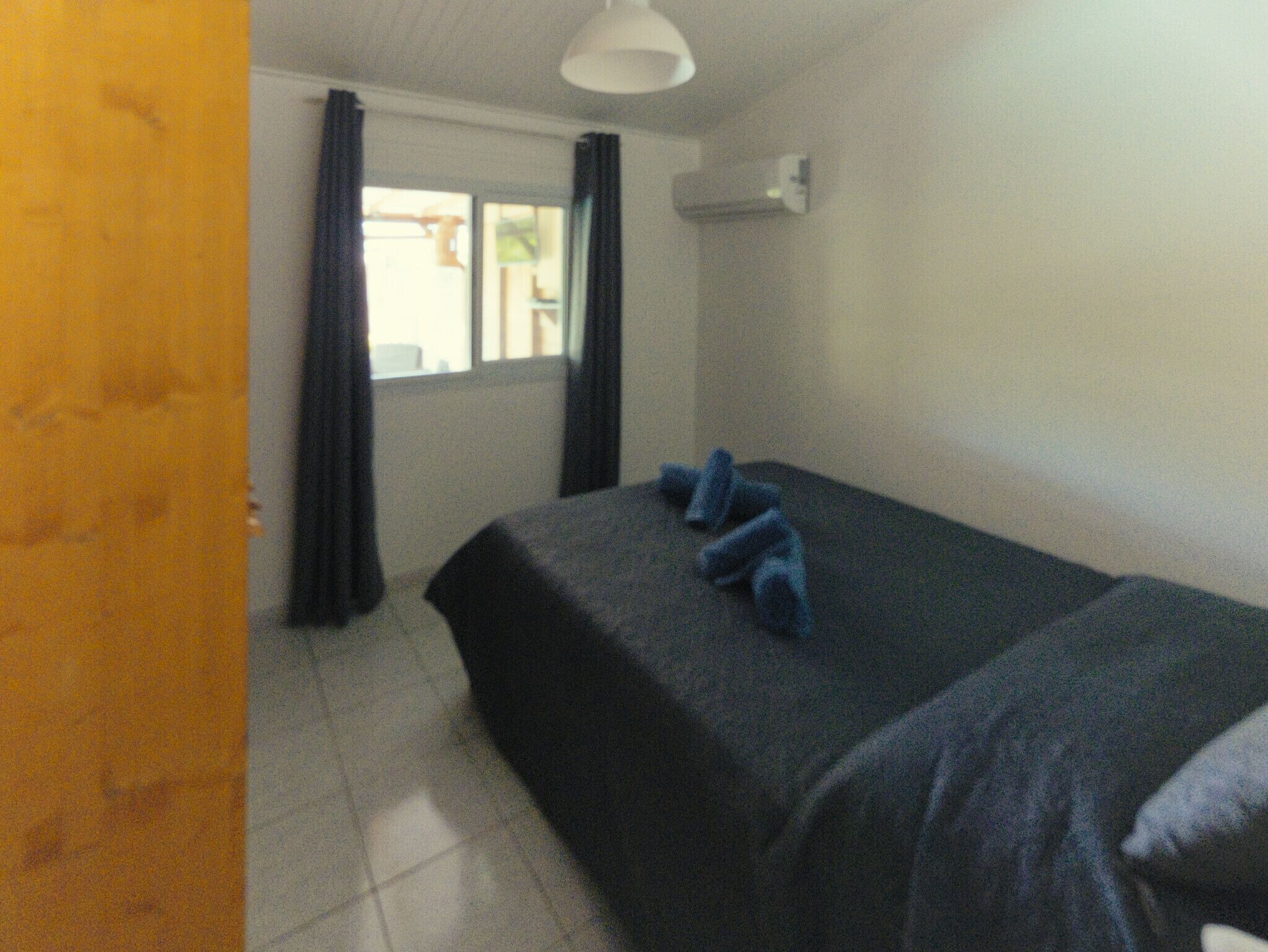 A small, simple room with a bed, a window with curtains, and a ceiling light.