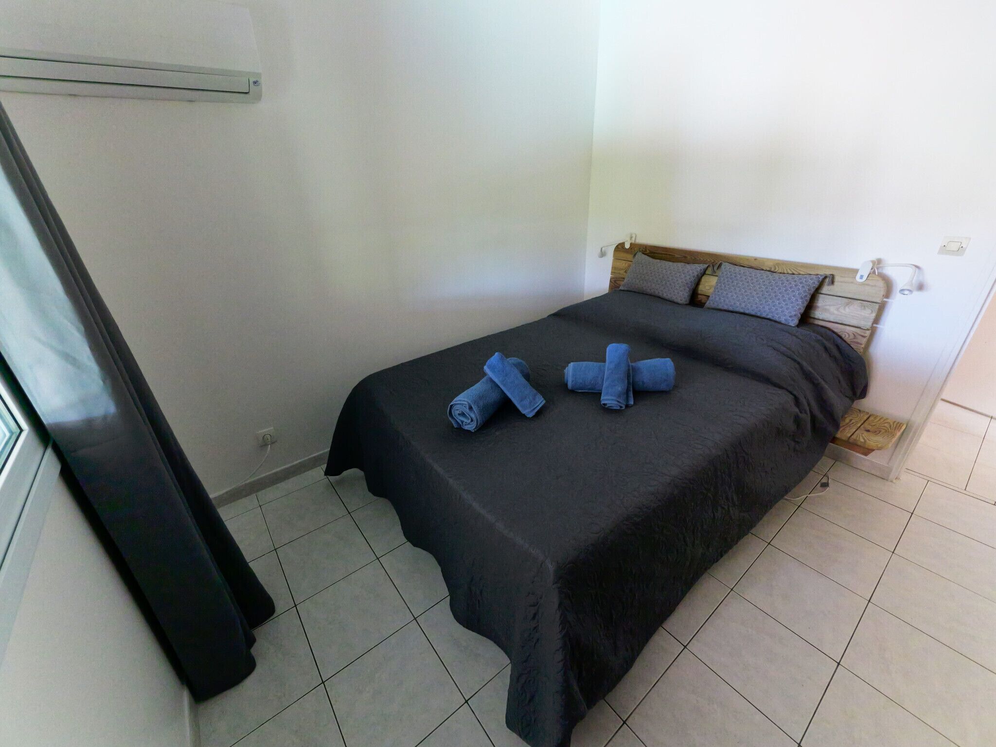Ein Einzelbett mit schwarzer Bettdecke und drei zusammengerollten Handtüchern.