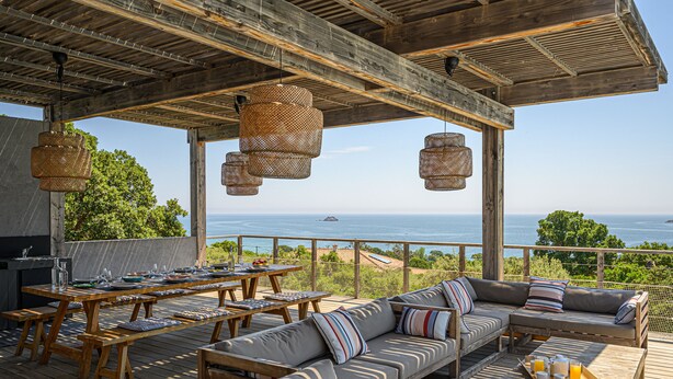 Una terraza al aire libre con mobiliario de madera, un sofá y lámparas de mimbre colgantes.