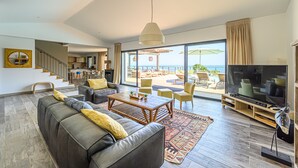 Amplia sala de estar con un sofá grande, una mesa de centro y un televisor. Cuenta con un balcón con mobiliario exterior y vistas al mar.