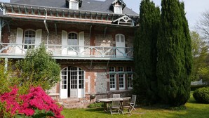 A two-story house with a balcony, a stone facade, and a well-maintained garden.