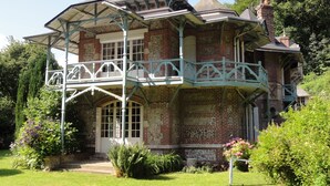 A large, historic building with a prominent balcony and a well-maintained garden.