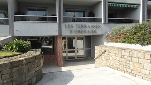 A building with a sign reading "LES TERRASSES D'EMER AUDE". It features a modern design with a glass entrance, stone walls, and a balcony with a green awning.
