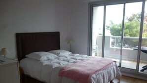 A bedroom with a bed, a nightstand, a lamp, and a view of the outdoors through a sliding glass door.
