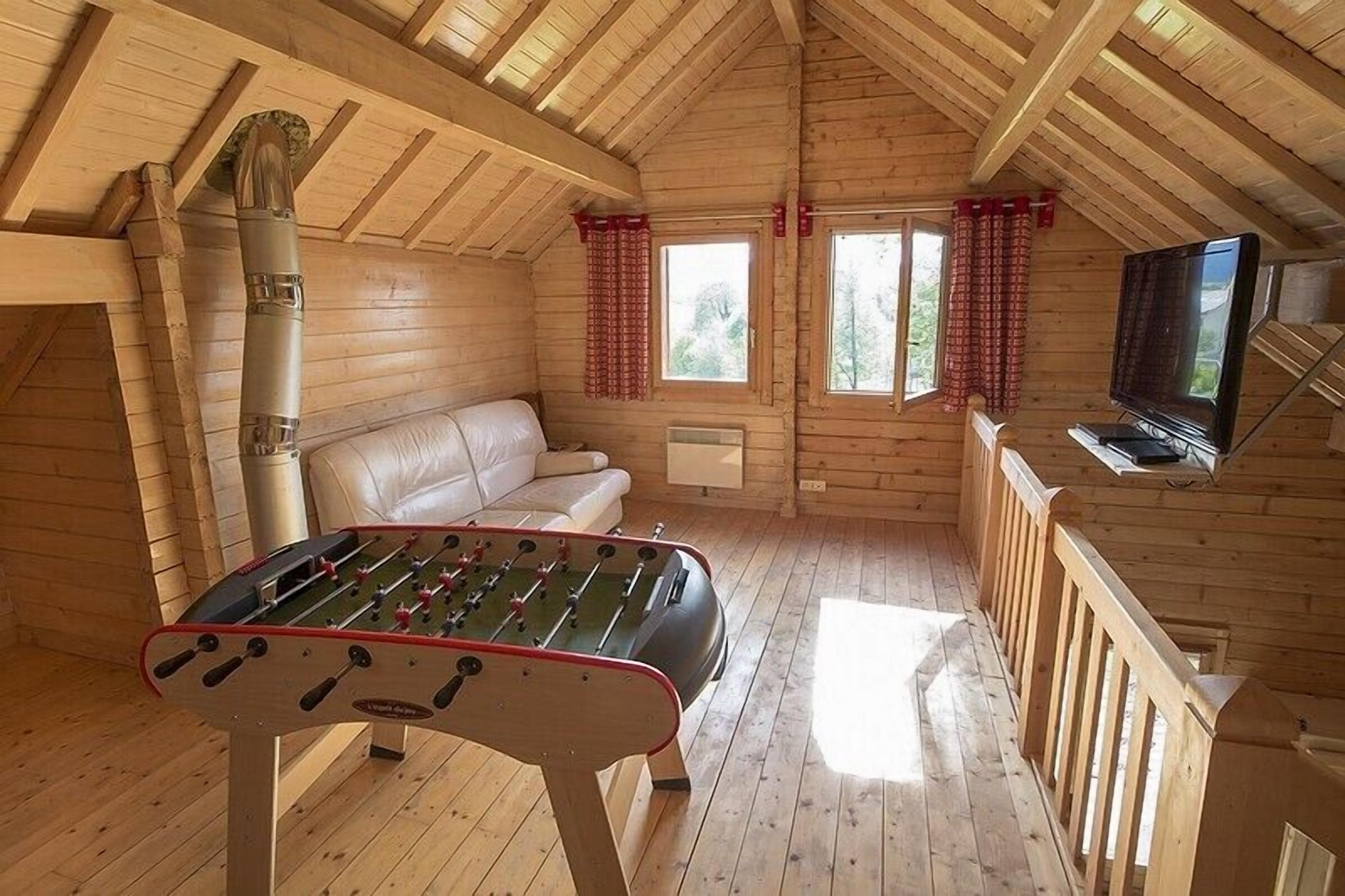 Een gezellig houten huisje met een tafelvoetbalspel, een bank en een televisie.