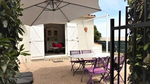 An outdoor patio with a table and chairs, a white umbrella, and a view of the interior through an open door. - Small house in the heart of nature, 4 km from Cargèse. (Cargèse)
