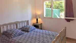 A bedroom with a bed, a nightstand, a lamp, and a window with curtains. - Small house in the heart of nature, 4 km from Cargèse. (Cargèse)