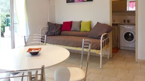 A living room with a sofa, a dining table with chairs, a washing machine, and a window with curtains. - Small house in the heart of nature, 4 km from Cargèse. (Cargèse)