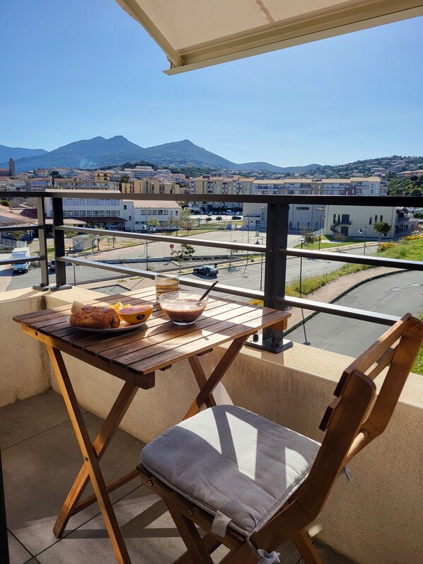 A balcony with a table, chairs, and a view of a cityscape and mountains. - PROPRIANO T2 2 steps from beaches All comforts, ideally located, quiet residence (Propriano)