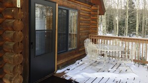 A log cabin with a wooden deck, a glass door, and a table with chairs. - Cabin Share Phase 2 (Angel Fire)