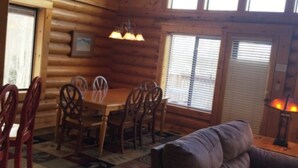 A cozy cabin interior with a wooden dining table, chairs, a sofa, and large windows. - Cabin Share Phase 2 (Angel Fire)