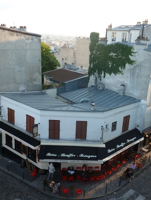 Un edificio con toldo negro, sillas y mesas rojas en el exterior.