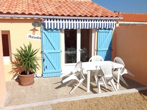 Un petit espace extérieur aménagé avec une table et des chaises, un pot de fleurs et un bâtiment doté d’une marquise bleue et d’une enseigne indiquant « Macomb ».