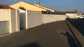 Eine Straße mit einer Betonmauer und einem Tor, ein geparktes Auto und ein Gebäude mit roten Ziegeln auf dem Dach.