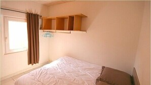 Ein Schlafzimmer mit einem Bett, einem Fenster mit Vorhängen und einem Holzregal darüber.