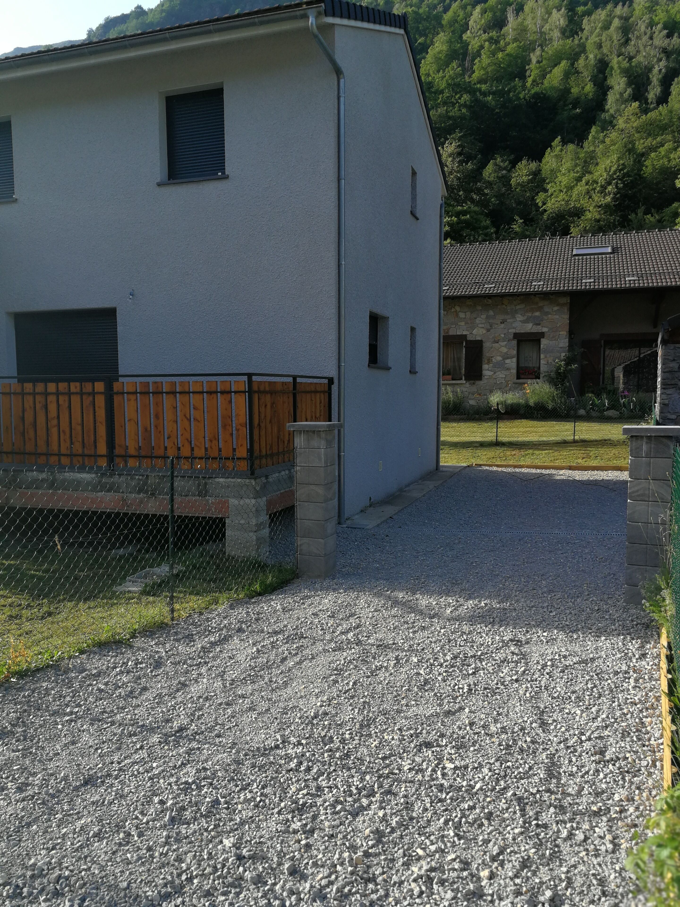 A modern building with a gravel driveway, a wooden fence, and a stone building in the background.