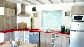 Moderni keittiö, jossa on punainen työtaso, ruostumattomasta teräksestä valmistetut kodinkoneet ja puiset keittiökaapit.