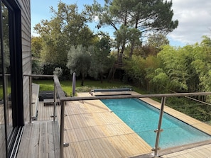 Una piscina con muelle de madera, rodeada de árboles y césped.