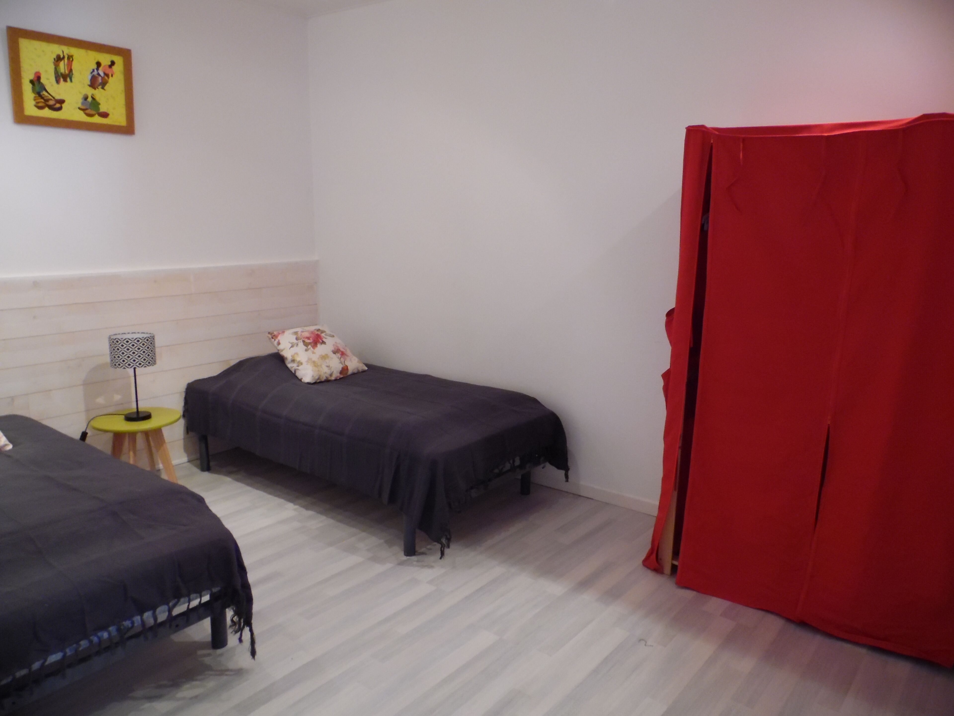 A room with two beds, a small table with a lamp, and a red curtain.