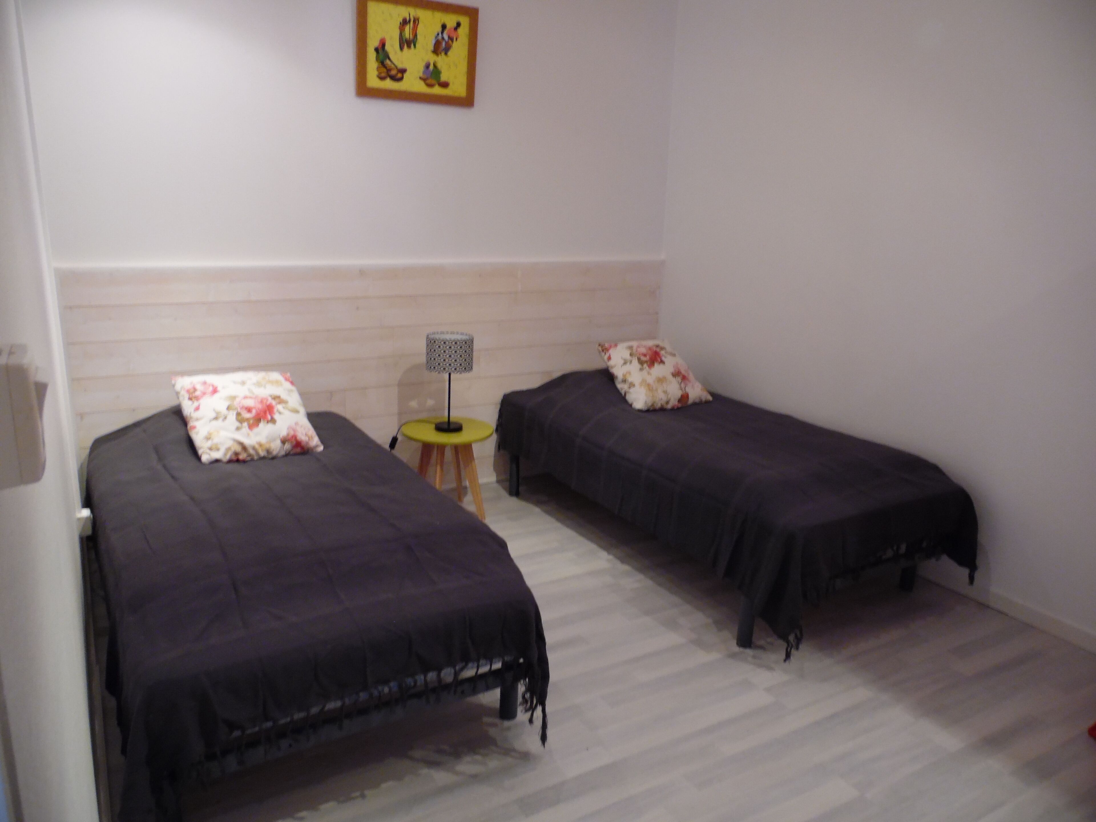 Ein Zimmer mit zwei Einzelbetten, jeweils mit einem floralen Kissen, einem kleinen runden Tisch mit einer Lampe und einem Bild an der Wand.