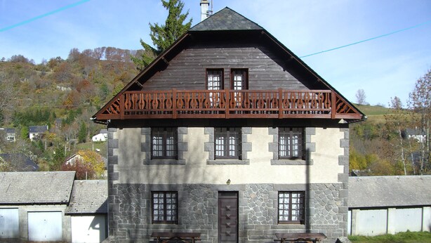 Ein zweistöckiges Steinhaus mit Balkon, mehreren Fenstern und einem Hauseingang.