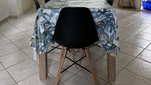 Ein Essbereich mit einem langen Tisch, bedeckt mit einer blumigen Tischdecke, umgeben von St ühlen, einer Kristallleuchter und einem Fenster mit Vorhängen.