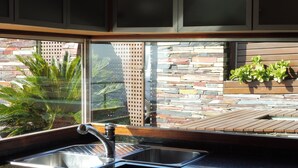 A kitchen with a large window, a sink, and a stone wall outside. - Luxury penthouse with terrace and jaquzzi the panoramic sea views (LLANÇA)