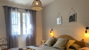 Un dormitorio con cama, mesita de noche, lámpara colgante y ventana con cortinas.