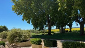 Un área de estar al aire libre con mesas y sillas, con vistas a un jardín ajardinado y campos.
