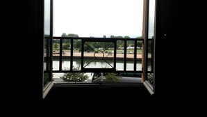 Blick aus einem Fenster mit Metallgeländer auf einen Fluss und entfernte Bäume.