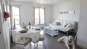 Ein modernes, helles Wohnzimmer mit einem weißen Sofa, einem Esstisch mit Stühlen und einem Hund, der auf dem Boden liegt.
