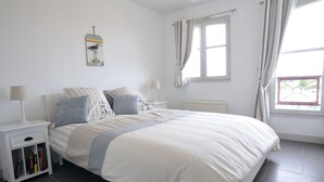 Ein Schlafzimmer mit Bett, Nachttischen, einem Fenster mit Vorhängen und einer Heizung.