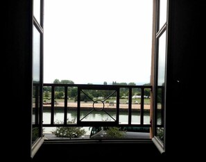Vista da janela com guarda-corrimão de metal, sobre o rio e árvores ao longe.