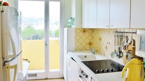 Una cocina con un amplio ventanal, armarios blancos, un fregadero, una estufa y diversos utensilios.