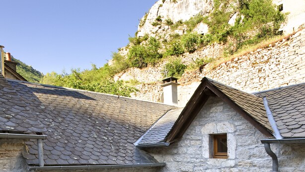 A stone building with a patio area featuring a table and chairs, surrounded by potted plants. - Beautiful vaulted house dating from 1647 (Jeanne's house) (La Malène)