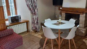 A cozy living room with a fireplace, a dining table with chairs, a sofa, a television mounted on the wall, and a window with curtains. - Beautiful vaulted house dating from 1647 (Jeanne's house) (La Malène)
