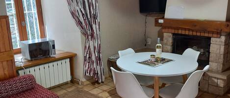 Una sala de estar acogedora con chimenea, una mesa de comedor con sillas, un sofá, un televisor montado en la pared y una ventana con cortinas.