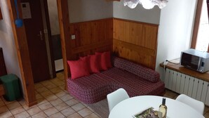 A cozy room with a wooden ceiling, a sofa with red cushions, a dining table with chairs, and a kitchen area with a microwave. - Beautiful vaulted house dating from 1647 (Jeanne's house) (La Malène)