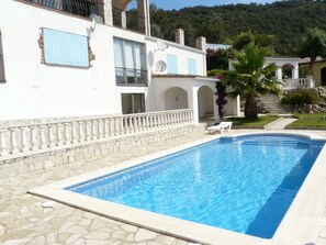 A swimming pool with stone tiles, a white building with blue shutters, and a stone wall. - Very pleasant villa on a hill, calm, with seesight, garden and private swimming (Calonge)